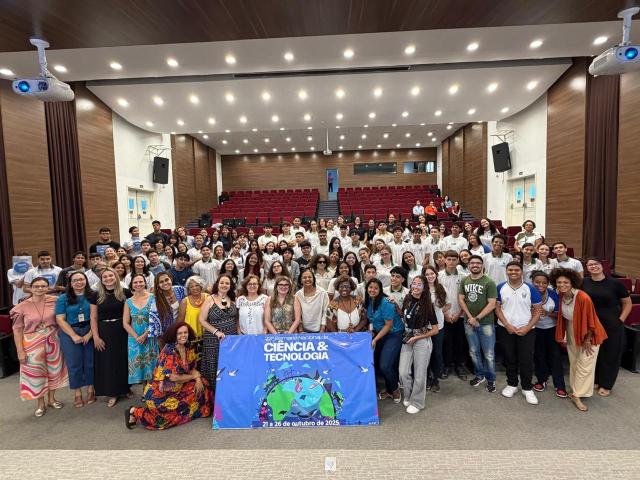estudantes e pesquisadores posam com o banner da Semana Naconal de Ciência e Tecnologia da Fiocruz, no auditório da regional Ceará.
