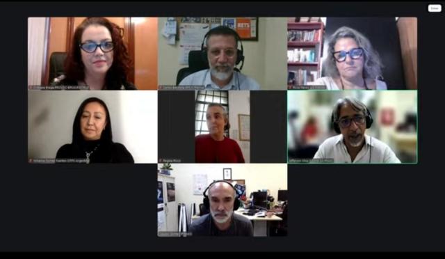Captura de tela de uma reunião virtual em formato de grade, exibindo sete participantes conectados por videoconferência. Cada pessoa aparece em seu próprio quadro, algumas usando fones de ouvido e microfone, em ambientes internos como escritórios ou salas de trabalho. 